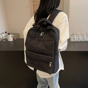 Detailed back view of a black quilted nylon backpack with zip pockets on a female model