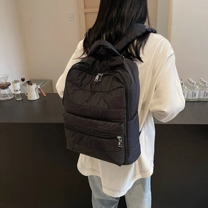 Close-up of a black quilted nylon puffer backpack worn by a model in a cozy cafe