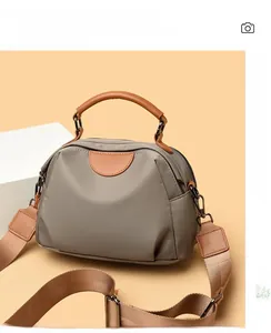 Detail of grey nylon shoulder bag with brown leather handles and adjustable fabric strap