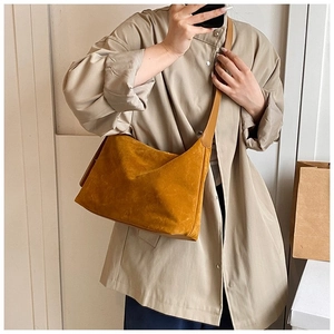 Détail d'un sac bandoulière en daim jaune moutarde porté à l'épaule sur un modèle