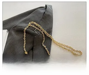 Detail der eleganten goldenen Metallkette der Abendtasche auf einem grauen Blazer