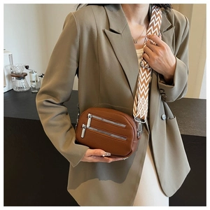 Brown leather crossbody bag with dual zippers and a colorful woven wide strap