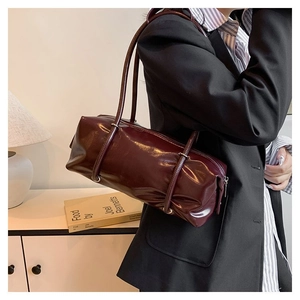 Detail of burgundy glossy PU leather Boston bag with modern cylindrical design and dual straps