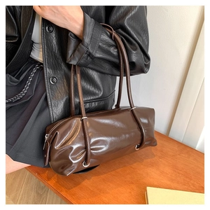 Detail of a dark brown glossy cylinder bag with sleek shoulder straps and leather texture