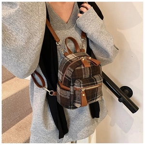 Detailopname van een mini-tartan rugzak met bruine kunstleren bies en goudkleurige hardware