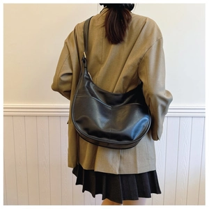 Detailed view of black synthetic leather hobo bag with adjustable strap worn by a model
