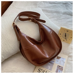 Detail view of brown leather hobo bag with white stitching and adjustable strap