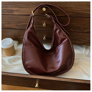 Detail of burgundy crescent handbag with vertical stitching placed in a wooden drawer