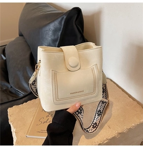 Detail of cream bucket bag featuring woven wide shoulder strap and front pocket stitching