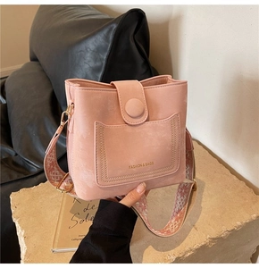 Pink bucket bag with wide geometric strap detail and gold buckle on a stone surface
