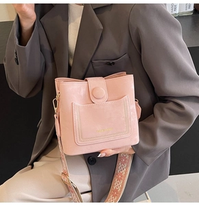 Close-up of pink bucket bag with wide ethnic style woven strap and fashion text detail