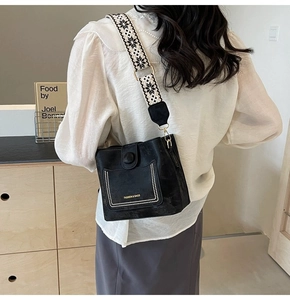 Black bucket bag with patterned wide strap worn by a model in an elegant indoor setting