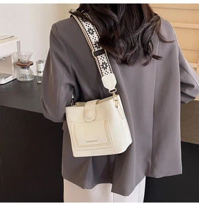 Close-up of white bucket bag with embroidered wide strap on model in cafe setting