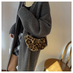 Detail of leopard print faux fur crescent bag with leather strap in cozy indoor setting