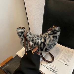 Chic leopard print faux fur crescent bag with brown leather strap on artistic background