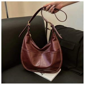 Minimalist burgundy semi-circle hobo bag in matte PU leather on a leather sofa