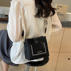 Chic black bucket bag with wide patterned shoulder strap worn by a model in a warm setting