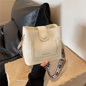 Off-white bucket bag with wide geometric woven shoulder strap on a stone display