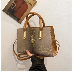 Detail der braunen Handtasche mit Krokodilmuster, Goldbeschlägen und glänzenden Lackseiten