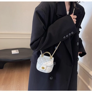 Détail du mini sac matelassé blanc avec poignée en métal doré sur un blazer