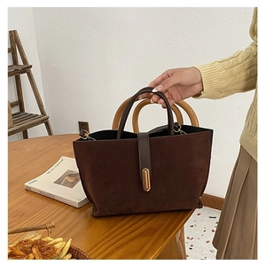 Close-up of brown suede handbag with leather handle and golden vertical lock detail