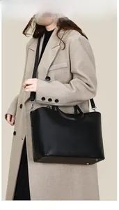 Detail of black PU leather tote bag with woven handles and adjustable shoulder strap on model