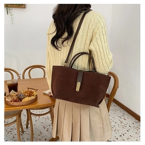 Detail of dark brown matte suede handbag with gold lock in a lifestyle setting