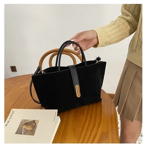Detail of black matte suede handbag with golden oval buckle on a wooden surface