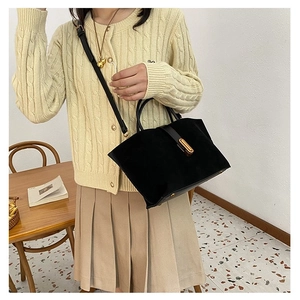Detail of a matte black handbag with a gold metal clasp worn by a model in a warm interior
