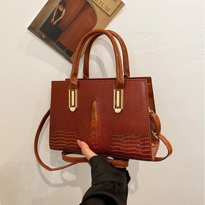 Detail der braunen Handtasche mit Krokodilmuster, goldener Hardware und Schultergurt