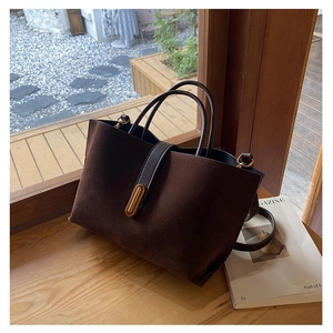 Detail of dark brown suede tote bag with golden capsule lock on a wooden windowsill
