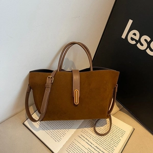 Close-up of caramel brown frosted suede tote bag with retro gold buckle on a vintage book