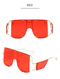 Close-up of red oversized shield sunglasses with gold metal frame and rivet detailing