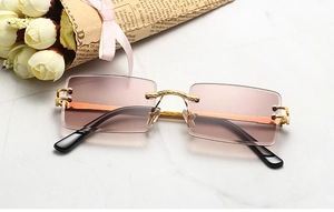 Detail of rimless rectangle sunglasses with pink gradient lenses and gold metal trim