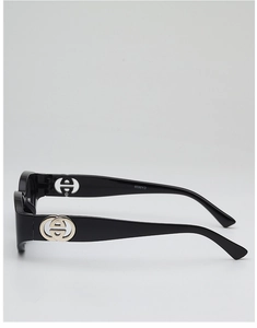 Detailed side view of black oval sunglasses featuring a golden interlocking metal logo on wide temples