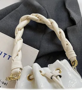 Detail of white glossy bucket bag featuring a thick woven handle and drawstring closure