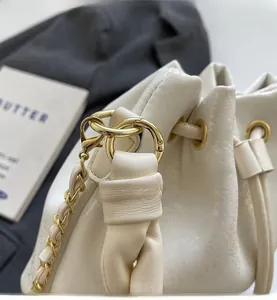 Detail of white bucket bag featuring pearlescent leather and gold metal hardware