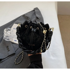 Detail of black drawstring bucket bag with cracked texture and gold chain ball charm