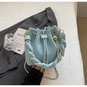 Close-up of light blue bucket bag with woven handle and gold chain strap on blazer