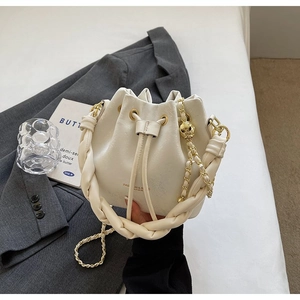 Detail of white drawstring bucket bag with gold ball chain and woven handle on a blazer