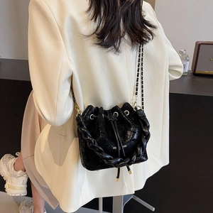 Detail of glossy black drawstring bucket bag with thick chain handle and metal shoulder strap