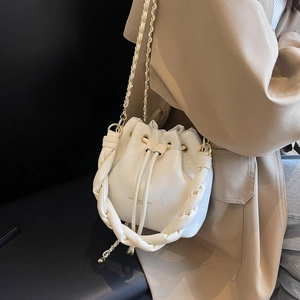 Detail of white leather bucket bag with woven handle and gold chain strap on shoulder