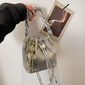Detail of silver bucket bag with braided handle and gold chain strap in hand