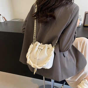 Detail of white drawstring bucket bag with braided handle and chain strap on a model