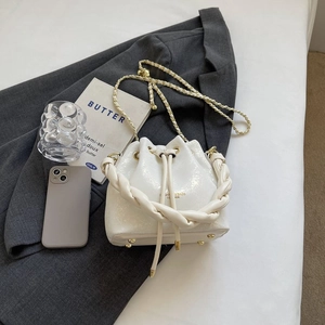 Detail view of white drawstring bucket bag with braided handle and gold metal chain strap