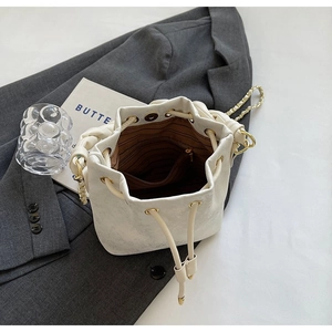 Chic cream white drawstring bucket bag with gold chain strap on a stylish grey background