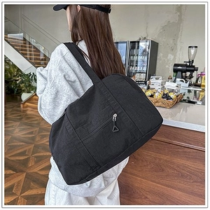 Dettaglio di una grande borsa tote in tela nera con tasca a zip indossata da una modella
