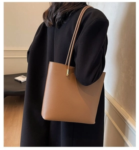Close-up of brown litchi grain leather tote bag with elegant gold metal strap accents