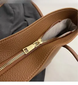 Detail of smooth gold zipper and grey herringbone lining on brown leather bag