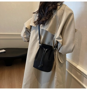 Detailed view of a black drawstring bucket bag worn over a beige trench coat